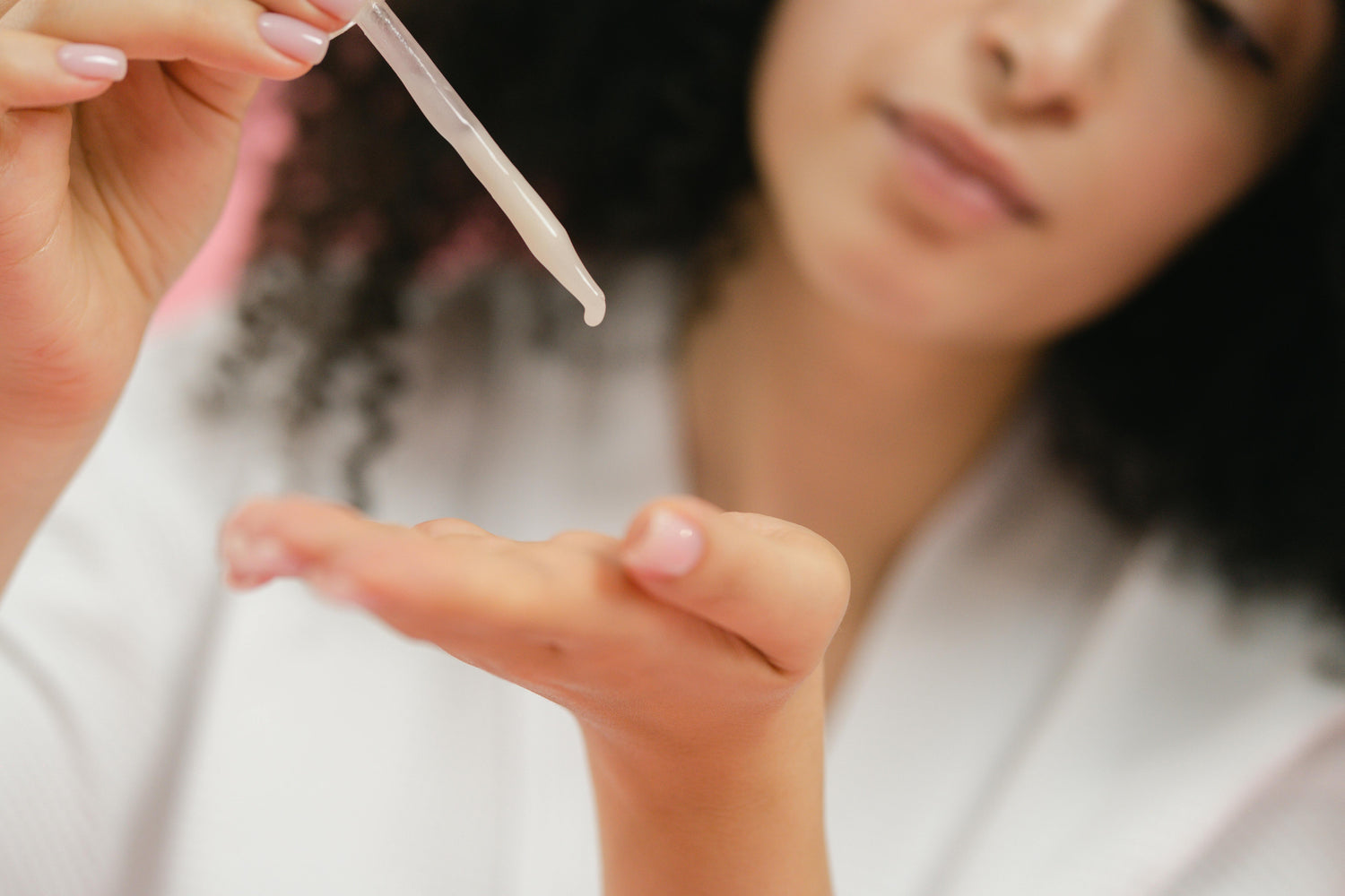 Close-up of a woman dispensing a lightweight skincare serum from a glass dropper onto her open palm, highlighting the product’s smooth texture and application.